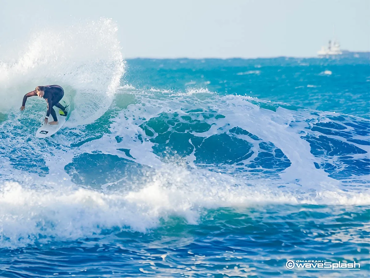 大きな波の斜面をハイスピードで滑走し、後方に力強い水飛沫を上げる佐藤李選手のライディング。