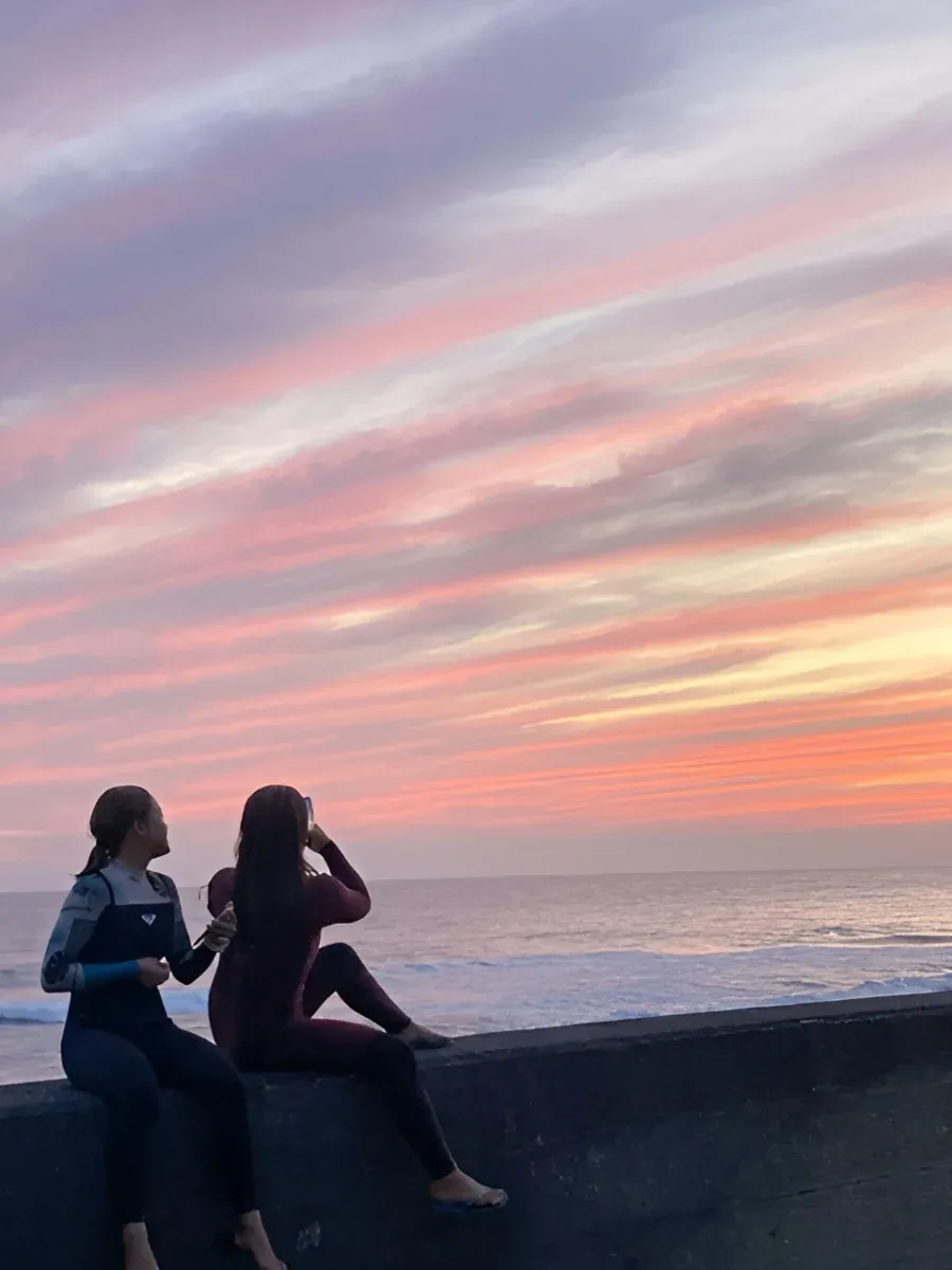 鮮やかな夕焼けに染まる御前崎の海辺で、堤防に座って遠くの水平線を眺める2人のシルエット。