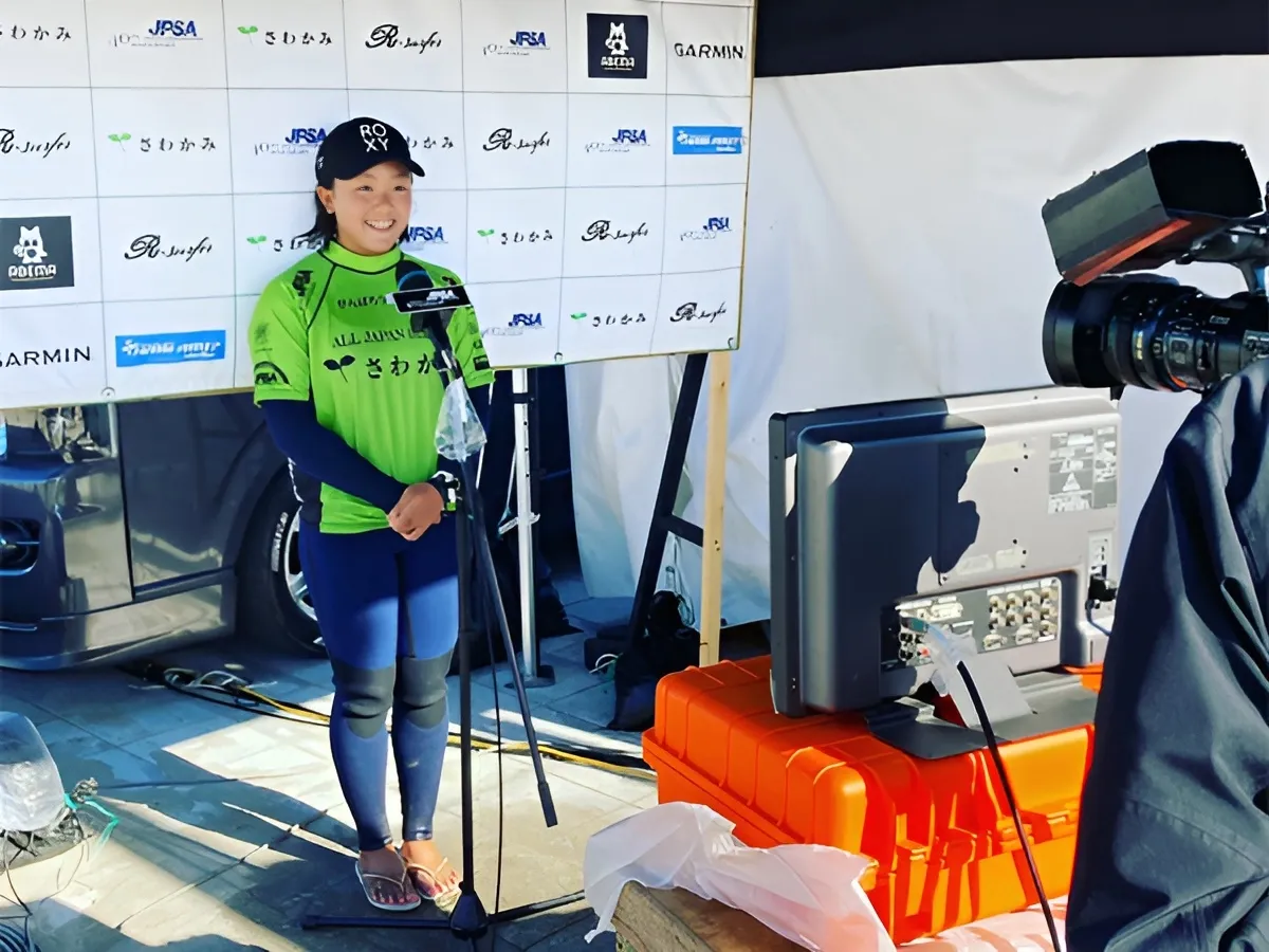 大会のバックボードの前で、多くのマイクやカメラに囲まれながらインタビューに応じる佐藤李選手。