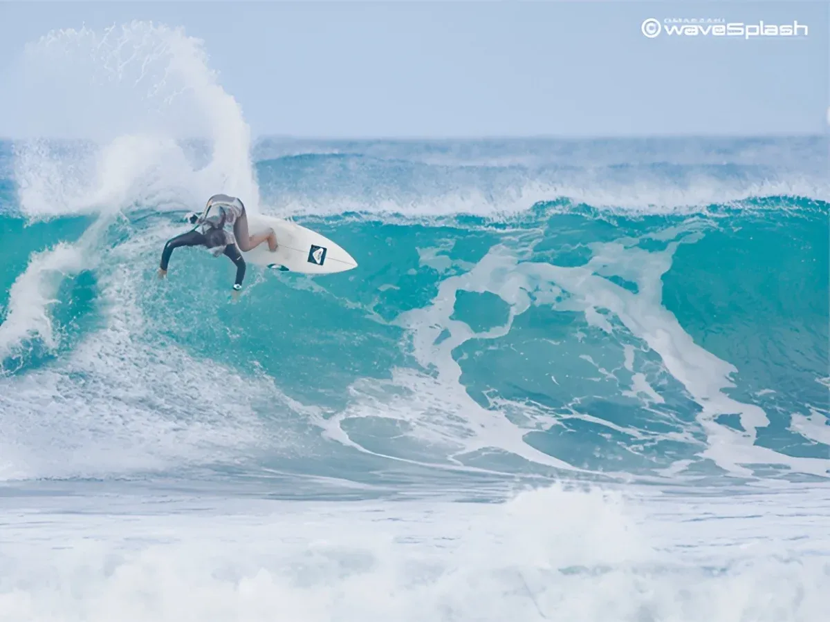 エメラルドグリーンの波の頂点で、白いサーフボードを深く傾けて鋭いターンを決める佐藤李選手。